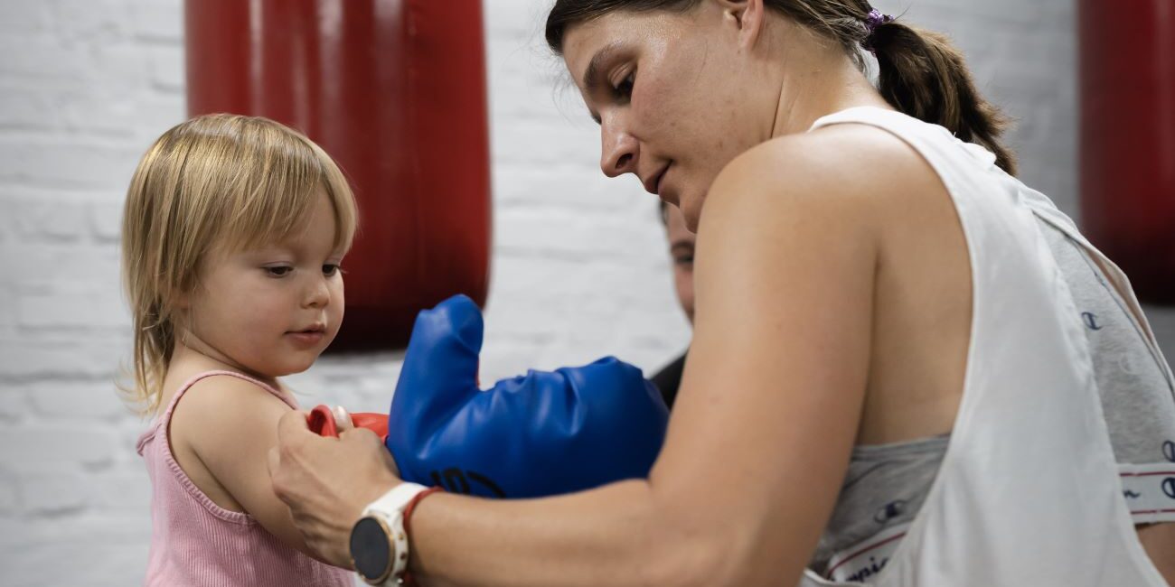 Gyerek bokszkesztyűt próbál fel felnőtt segítséggel a PiroskaGymben Bükön, családbarát közegben.