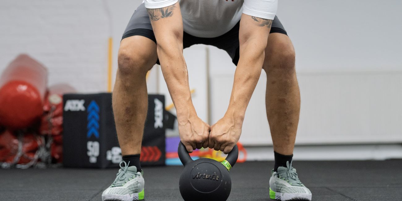 Kettlebell swing: sportoló két kézzel emeli a kettlebellt a talajról – PiroskaGym Bük.