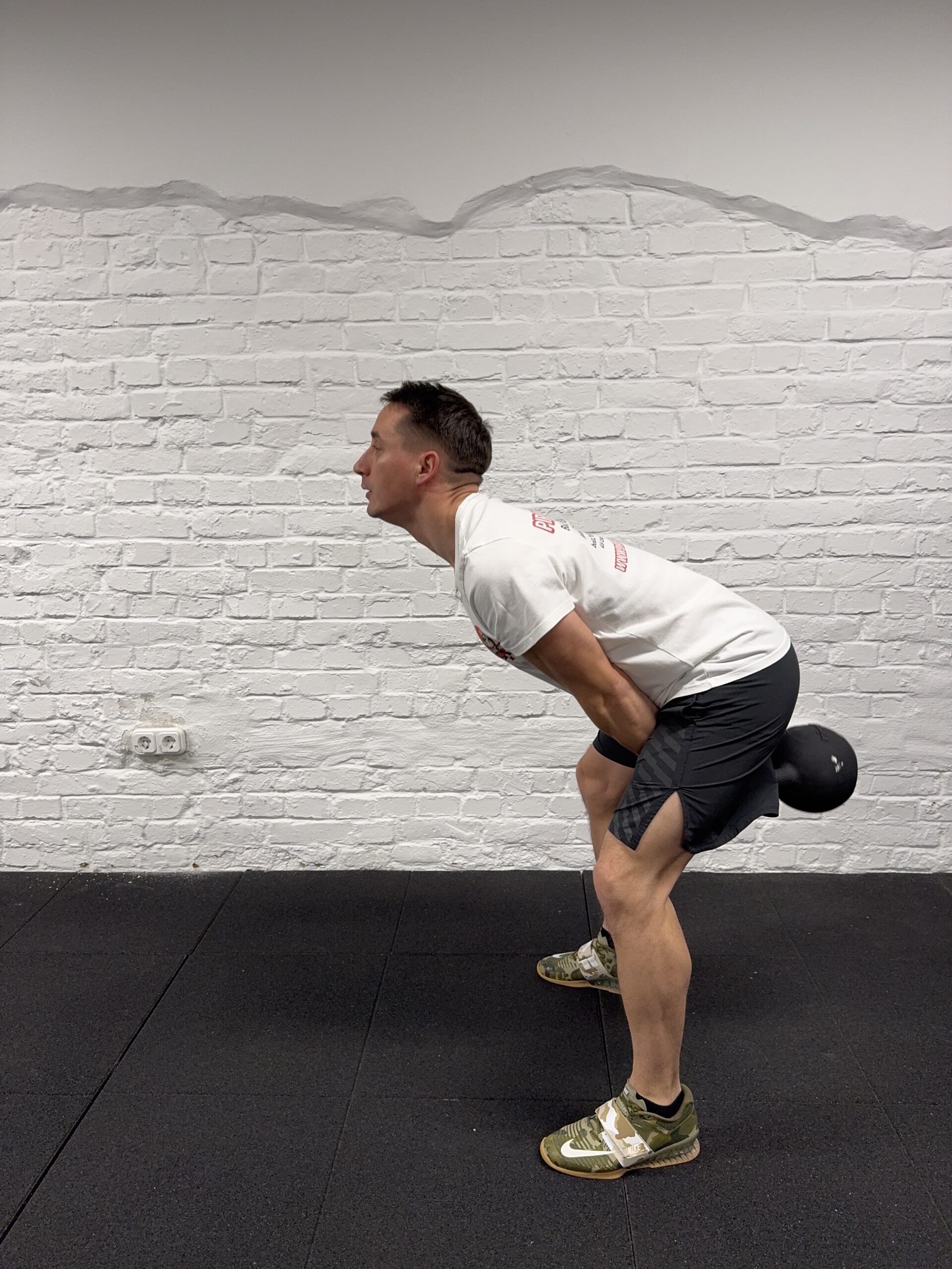 Kettlebell swing alsó pozíció oldalnézetből: csípő hátra, semleges hát, a bell a lábak között.